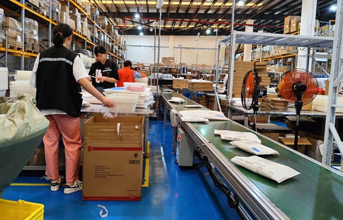 The staff are busy in the warehouse, organizing and packaging products, and the goods are transported by conveyor belts, demonstrating efficient logistics and warehousing operations