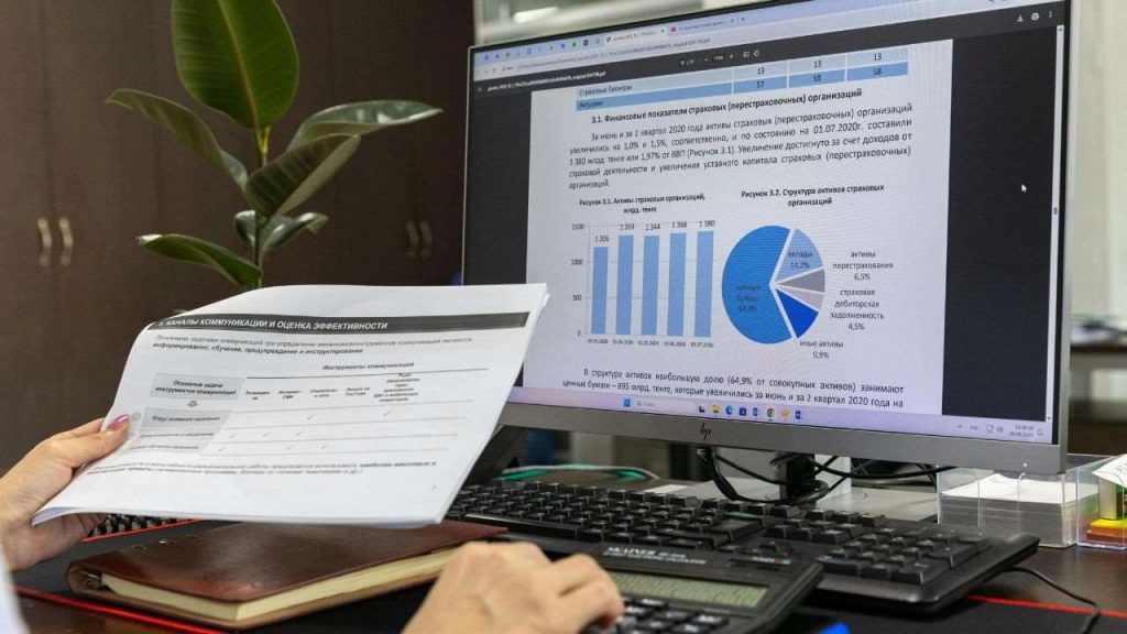 An image showing an analysis of high conversion rate product page structures on a computer screen. The display features graphs and charts detailing financial indicators and activity structures, with a person holding a document in hand. A plant is visible in the background, adding to the office setting, indicating a focus on effective communication and evaluation in product marketing strategies.