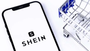 Shein logo on smartphone with mini shopping cart — a symbolic image representing the dominance of Shein in fashion eCommerce and why sellers are searching for similar sites like Shein.
