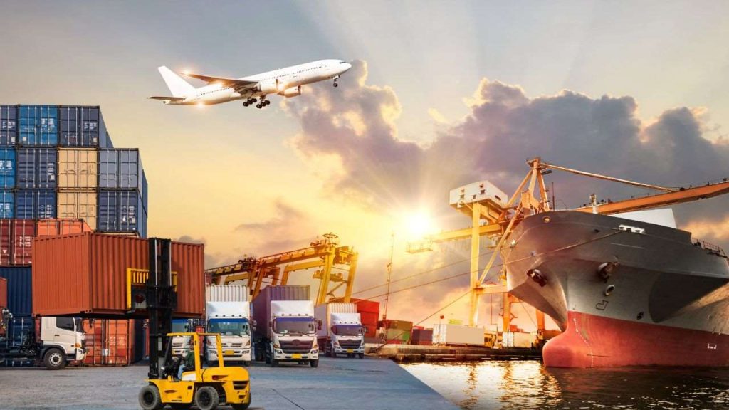 An image showcasing a busy logistics and shipping hub, featuring stacked shipping containers, trucks, and a cargo ship at dock. An airplane is flying overhead, representing international transport. The scene is illuminated by a warm sunset, highlighting the dynamic operations involved in global logistics and freight management.